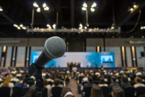 microphone-with-abstract-blurred-photo-of-conference-hall-or-meeting-room-with-attendee-background.jpg